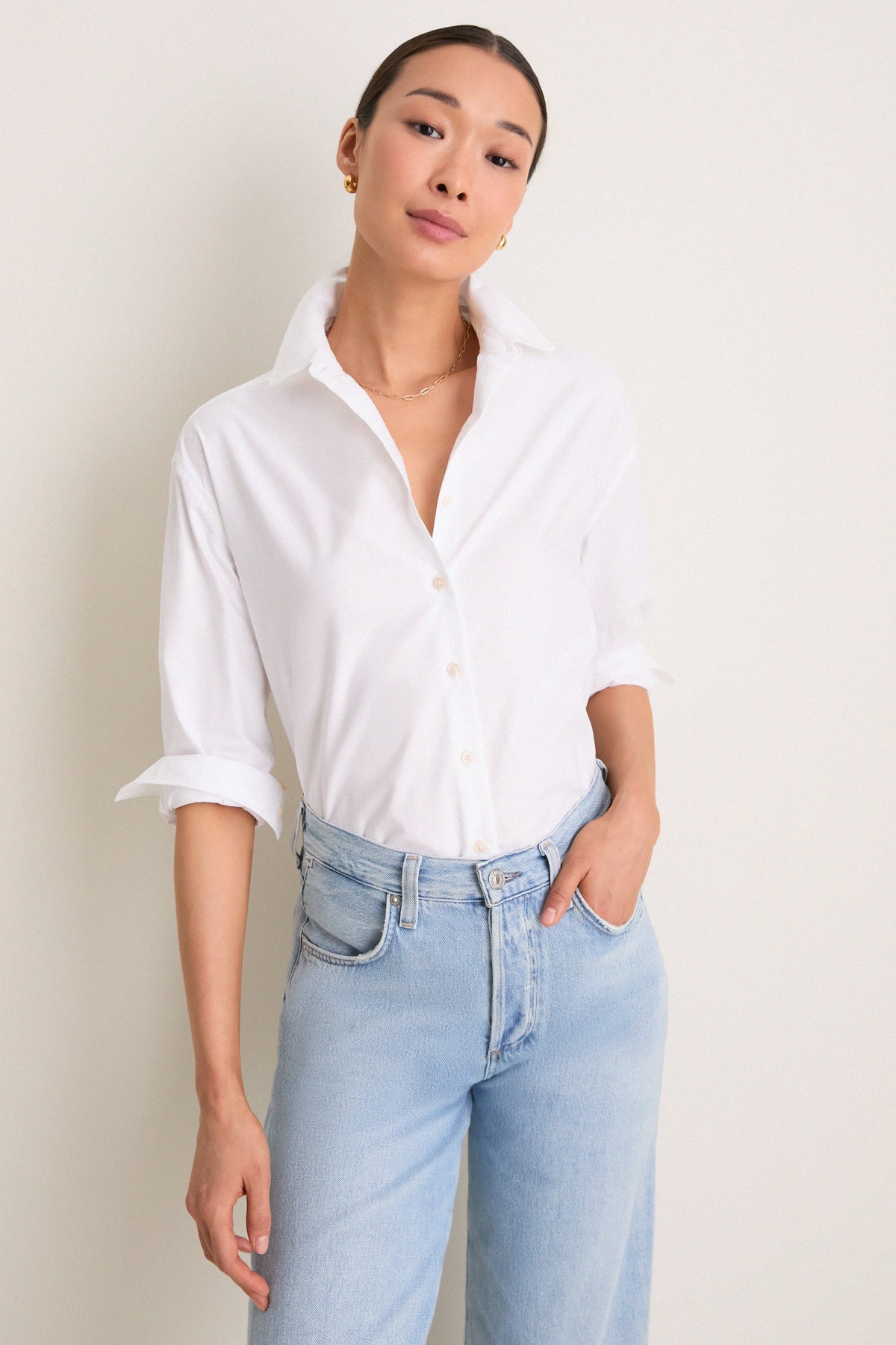 White oxford button-down shirt with sleeves rolled, worn with light blue jeans