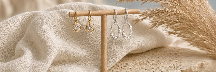 Crystal_pendant_drop gold earrings, and Silver_hoop_dops on wood stand with Cream linen cloth behind on a stone table with pampas grass decor