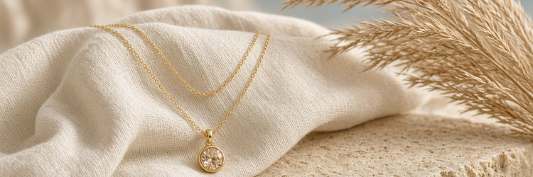 Crystal pendant on a 14kt gold chain, layered with a second gold chain on a piece of cream linen and stone table with pampas grass table decor