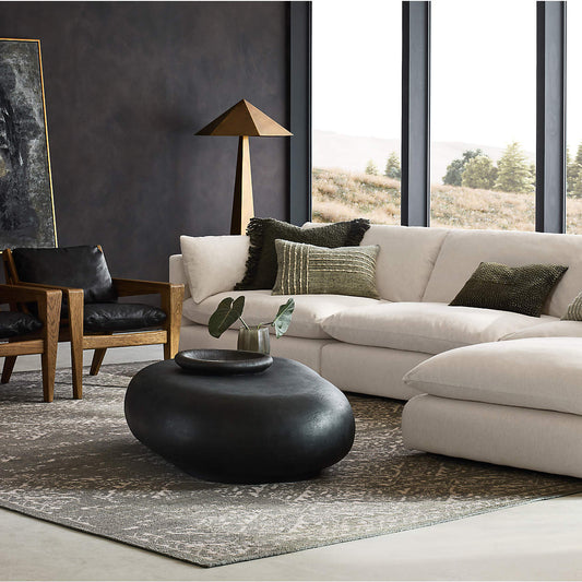 Brass geometric floor lamp in living room with a beige sectional sofa, black coffee table, and armchair.