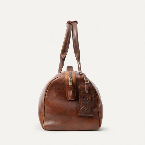 Leather travel duffle bag in Cognac shown in a coastal ranch setting-end view