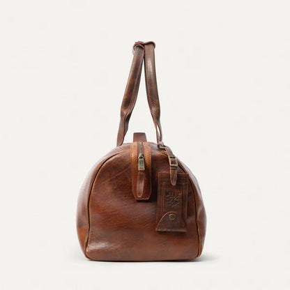Leather travel duffle bag in Cognac shown in a coastal ranch setting-end view