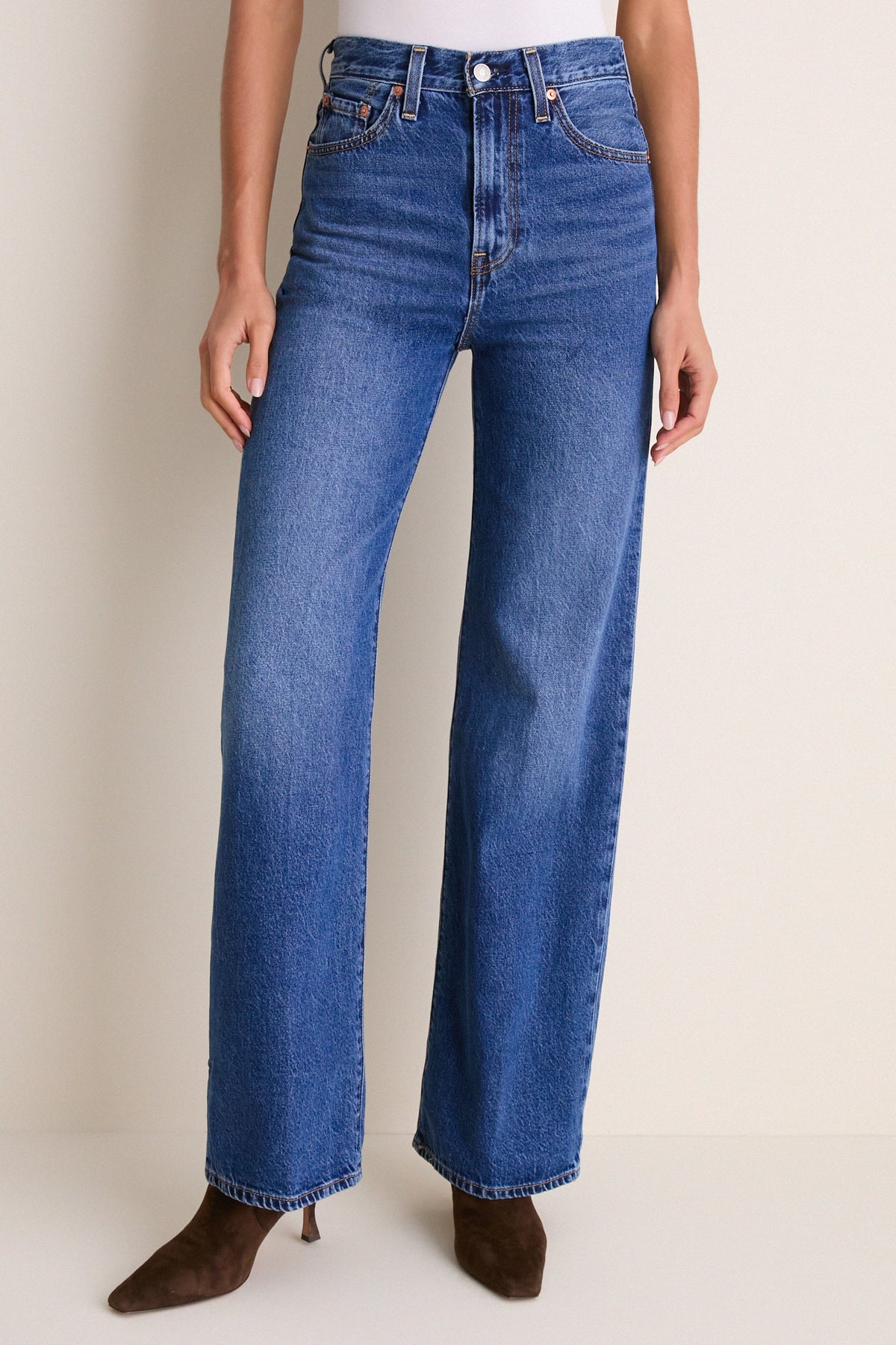Front view of a high-rise wide leg jean in a medium blue wash, worn with brown pointed-toe boots