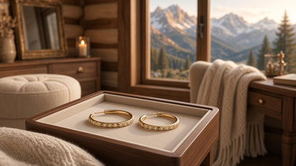 14K gold hoop earrings crystal. lifestyle view of 14K gold hoop earrings with crystal detail resting in a wooden tray inside a cozy mountain cabin with mountain views, props not included