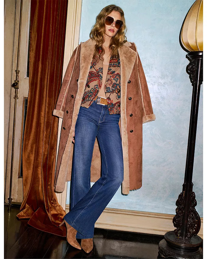 Engraved buckle western belt  model wearing a long brown coat, patterned top, and blue jeans indoors.