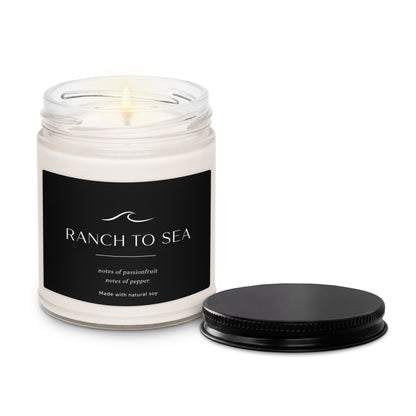 Candle in a glass jar labeled with a black Ranch To Sea  label with black lid on a white background.